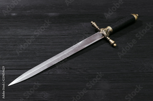 Dagger knife isolated on the black wooden background.