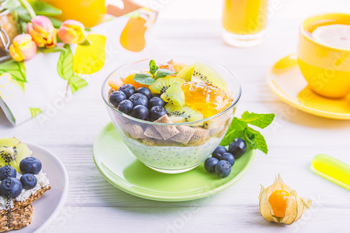 Yogurt with chia seeds, corn pads, kiwi, blueberries, physalis and mint on a background