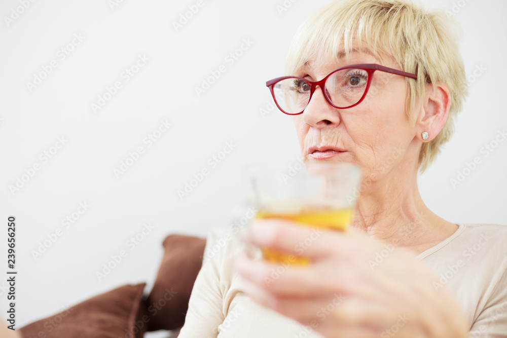 Worried senior woman lying in bed and drinking tea while recovering from illness. Worried senior woman lying in bed and drinking tea while recovering from illness.