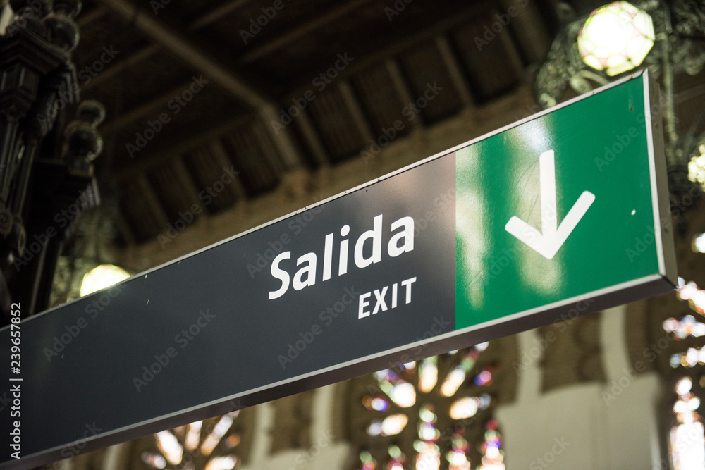Obraz premium Image of a Train station is seen on the image. The shade is seen too. Train is an important part of transportation in Spain. An Exit text sign is seen in both English and Spanish language