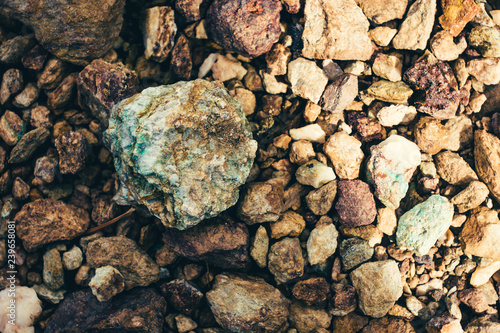 Raw ore on ground close-up. Multicolor rough stone in sunlight. Textured vivid geological background with pile of rude stones. Natural texture with copy space. Amazing mineral. Piece of rock.