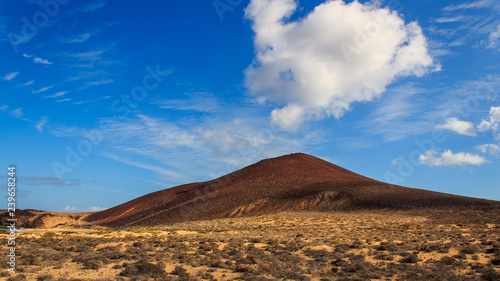 Volcanic mountain on a sunny summer day under an intense blue sky with fluffy white clouds. Scenery on La Graciosa Island, Canary, Spain.