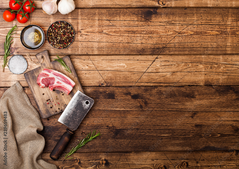 Fresh raw butchers lamb beef cutlets on chopping board with vintage meat hatchet on wooden background.Salt, pepper and oil with tomatoes and garlic and barbeque sauce