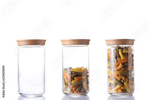 therre glass jar, one empty, one half empty and one full of colored raw pasta isolated on white background with clipping path and copy space for your text