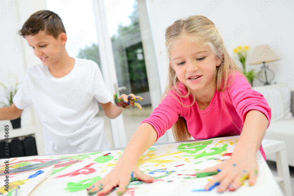 Fototapeta premium two beautiful young kids boy and girl hand painting on a white paper with color paint