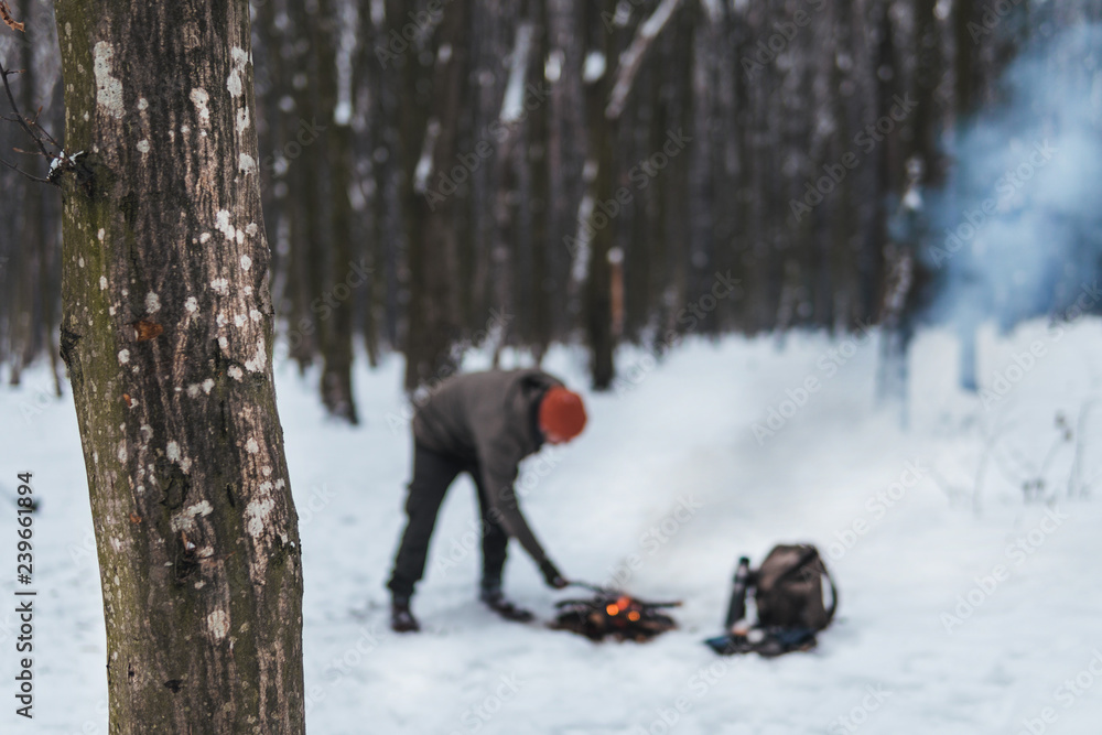 Traveling man makes a fire. Winter time. Concept adventure active vacations outdoor. Extreme camping. vintage backpack and thermos with tea, snowy forest Traveling man makes a fire. Winter time. Concept adventure active vacations outdoor. Extreme camping. vintage backpack and thermos with tea, snowy forest