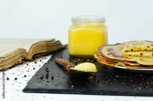 Pancakes roasted on a tray are plentifully covered with butter and a wooden spoon with butter photo