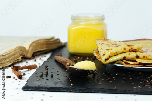 Pancakes roasted on a tray are plentifully covered with butter and a wooden spoon with butter photo