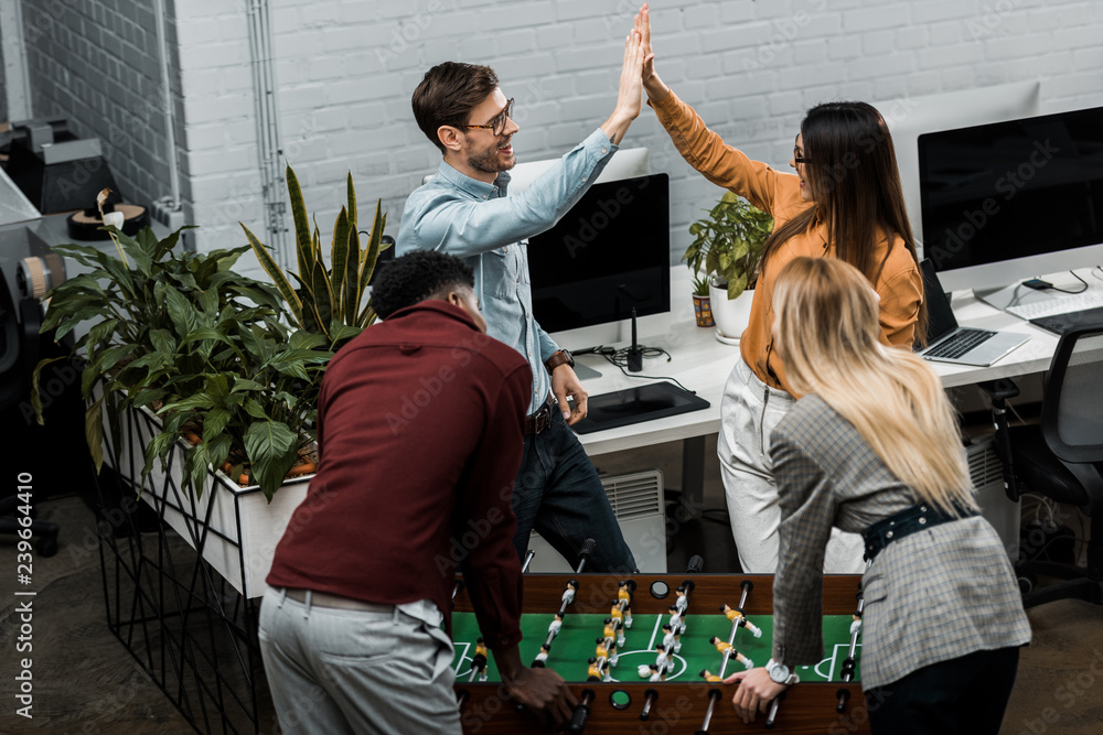 multicultural business colleagues playing table football together in office