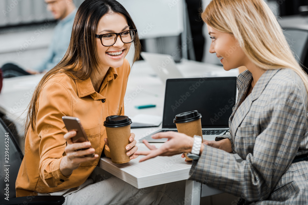 cheerful businesswomen using smartphone together at workplace in office cheerful businesswomen using smartphone together at workplace in office