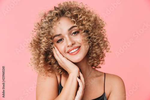 Portrait closeup of gorgeous curly woman 20s wearing dress smiling while standing, isolated over pink background