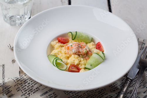 Omelette stuffed with salted salmon on a white plate on wooden white background.
