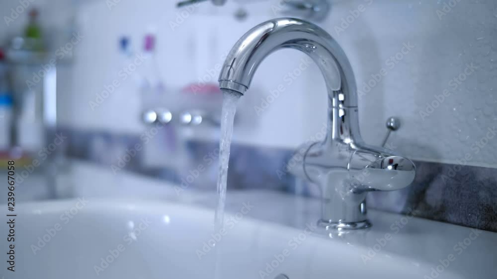 In the bathroom, the hand opens ( closing ) the water tap and water starts to flow from the faucet into the washbasin. Closeup In the bathroom, the hand opens ( closing ) the water tap and water starts to flow from the faucet into the washbasin. Closeup