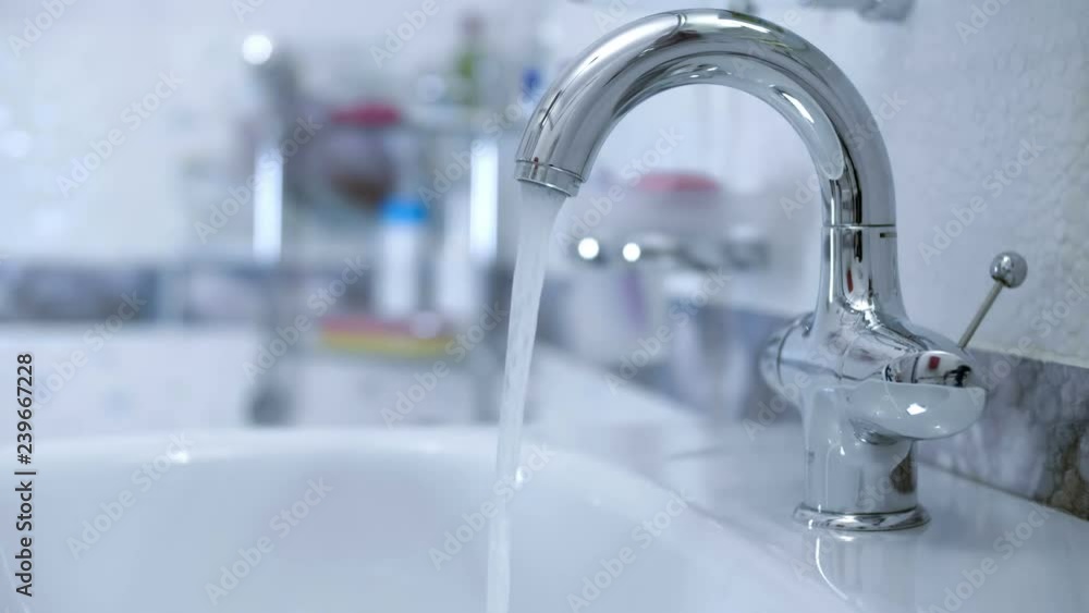 In the bathroom, the hand opens ( closing ) the water tap and water starts to flow from the faucet into the washbasin. Closeup In the bathroom, the hand opens ( closing ) the water tap and water starts to flow from the faucet into the washbasin. Closeup