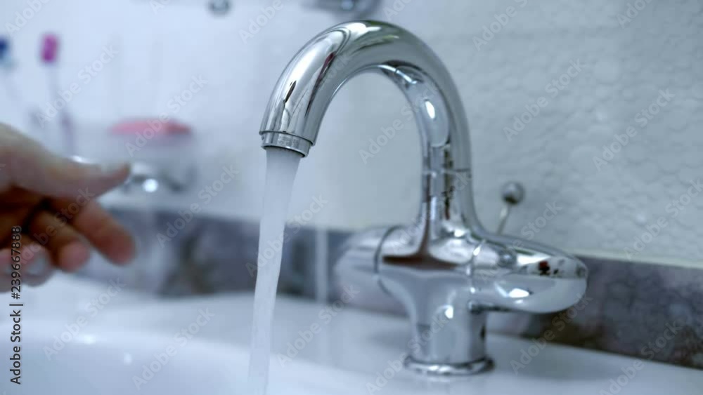 In the bathroom, the hand opens ( closing ) the water tap and water starts to flow from the faucet into the washbasin. Closeup. Shot in motion In the bathroom, the hand opens ( closing ) the water tap and water starts to flow from the faucet into the washbasin. Closeup. Shot in motion