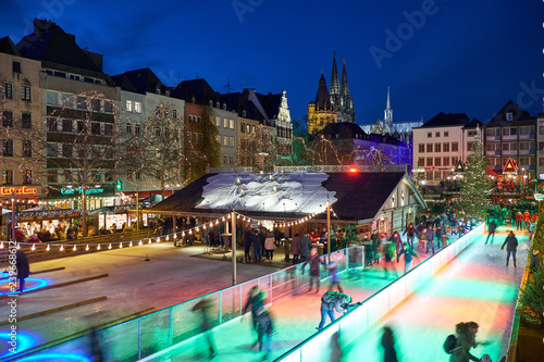 Weihnachtsmarkt in Köln am Heumarkt bei Nacht. Sicht auf die Eisbahn auf der Besucher Schlittschuh laufen können.