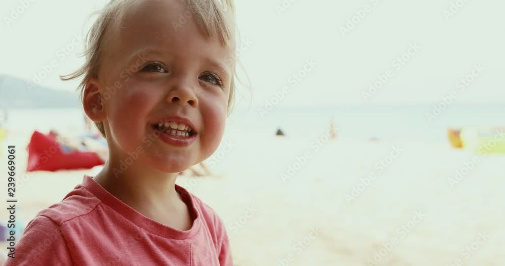 Adorable little child smiling while standing on background of sandy beach and sea on sunny daytime Adorable little child smiling while standing on background of sandy beach and sea on sunny daytime