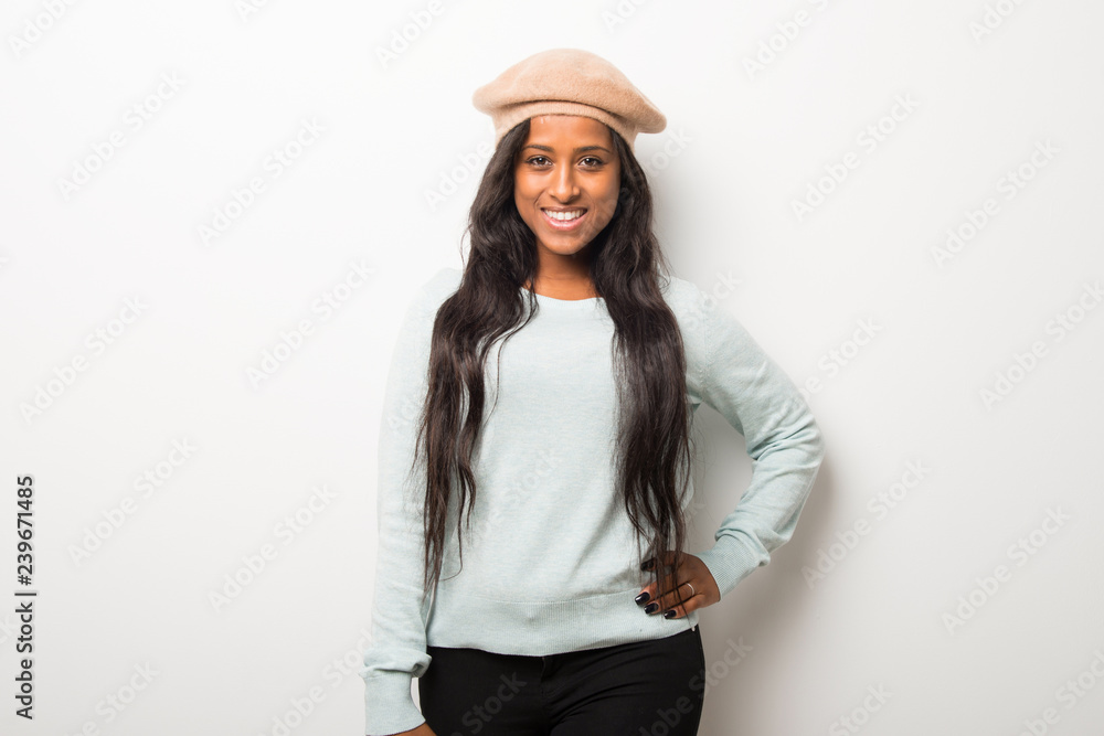 Young afro american woman on white wall posing with arms at hip and smiling Young afro american woman on white wall posing with arms at hip and smiling
