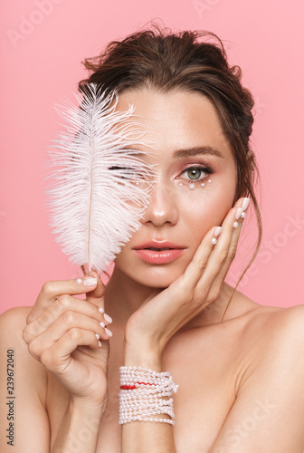Beautiful young woman posing isolated over pink wall background holding feather leaf.