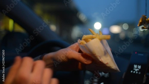 A man eats a French Fries Potato from McDonalds sitting in a Car at Night