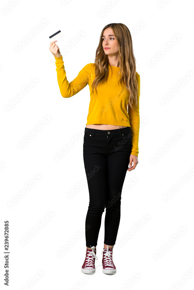A full-length shot of a young girl with yellow sweater taking a credit card without money on isolated white background A full-length shot of a young girl with yellow sweater taking a credit card without money on isolated white background