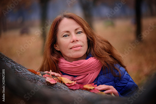 girl in a red scarf stands near a tree in autumn park full of colorful flowers