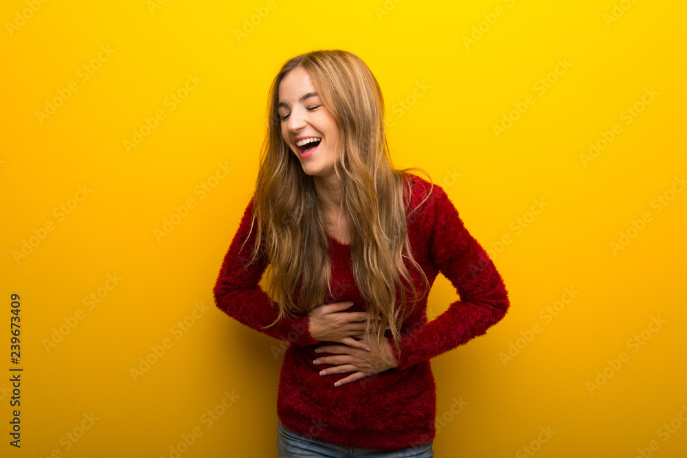 Young girl on vibrant yellow background smiling a lot while putting hands on chest