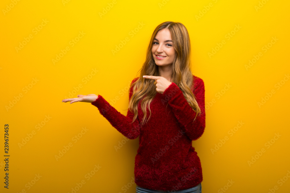 Young girl on vibrant yellow background holding copyspace imaginary on the palm to insert an ad Young girl on vibrant yellow background holding copyspace imaginary on the palm to insert an ad