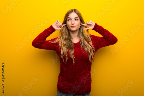 Young girl on vibrant yellow background covering both ears with hands