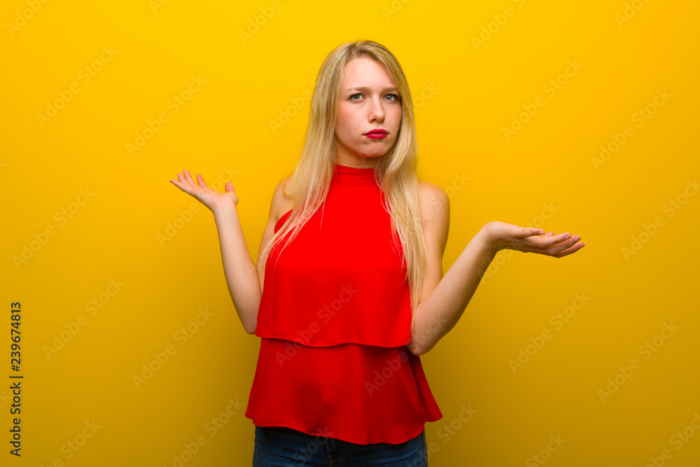 Young girl with red dress over yellow wall unhappy and frustrated with something because not understand something Young girl with red dress over yellow wall unhappy and frustrated with something because not understand something