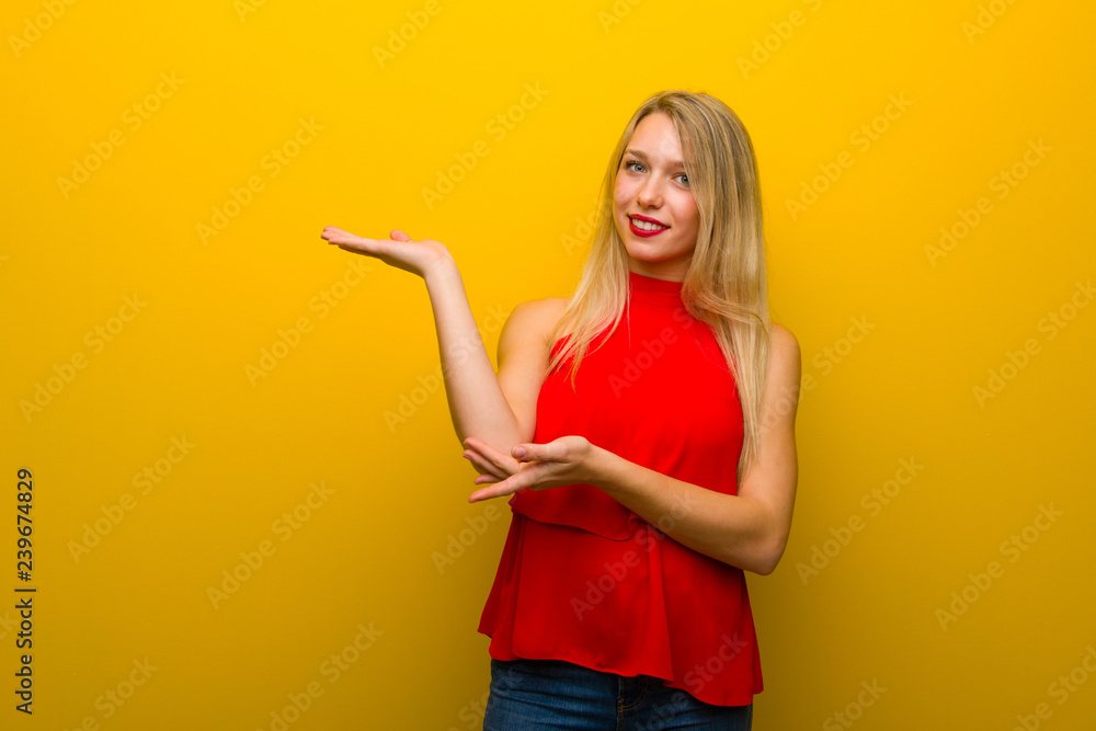 Young girl with red dress over yellow wall extending hands to the side for inviting to come Young girl with red dress over yellow wall extending hands to the side for inviting to come