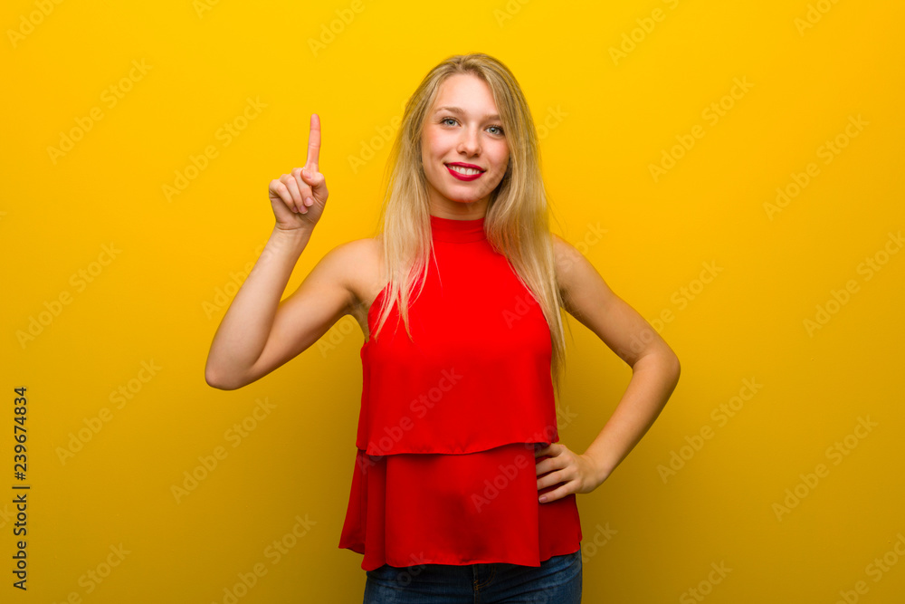 Young girl with red dress over yellow wall showing and lifting a finger in sign of the best Young girl with red dress over yellow wall showing and lifting a finger in sign of the best