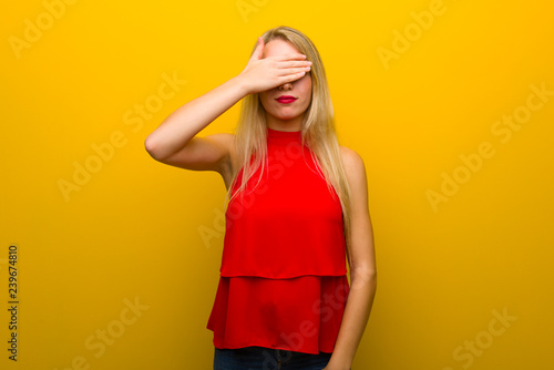 Young girl with red dress over yellow wall covering eyes by hands. Do not want to see something