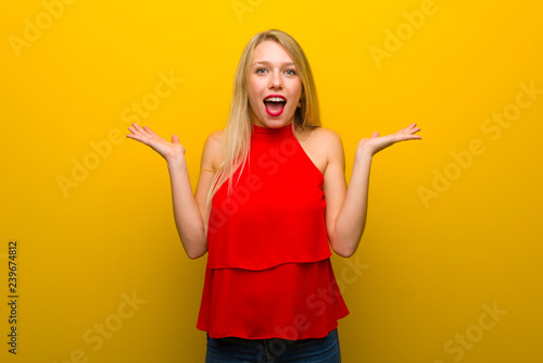 Young girl with red dress over yellow wall with surprise and shocked facial expression