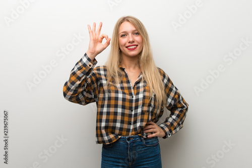 Blonde young girl over white wall showing an ok sign with fingers