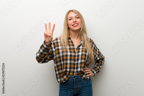 Blonde young girl over white wall happy and counting three with fingers
