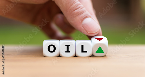 Hand is turning a dice and changes the direction of an arrow symbolizing that the Oil price is changing the trend and goes down instead of up (or vice versa) 
