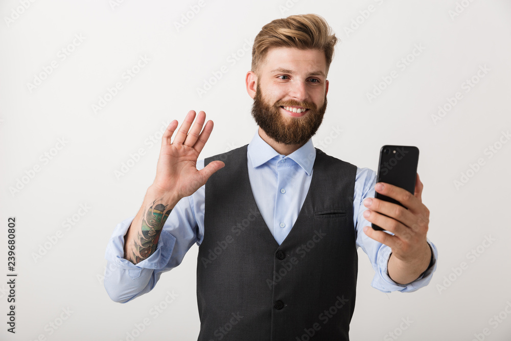 Handsome young bearded man standing isolated over white wall background using mobile phone. Handsome young bearded man standing isolated over white wall background using mobile phone.