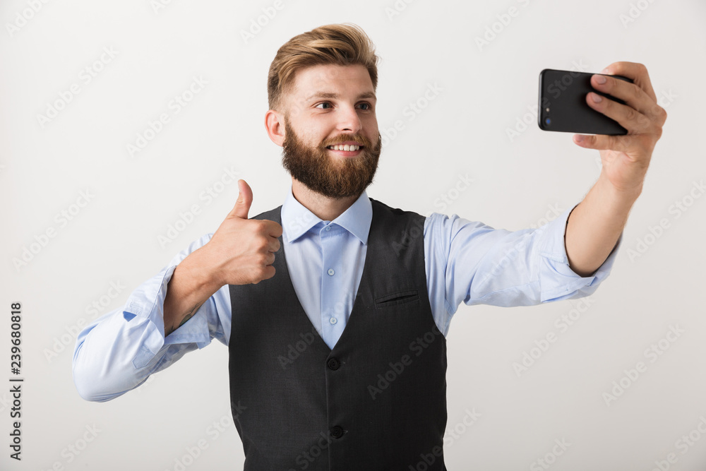 Handsome young bearded man standing isolated over white wall background take a selfie by mobile phone. Handsome young bearded man standing isolated over white wall background take a selfie by mobile phone.