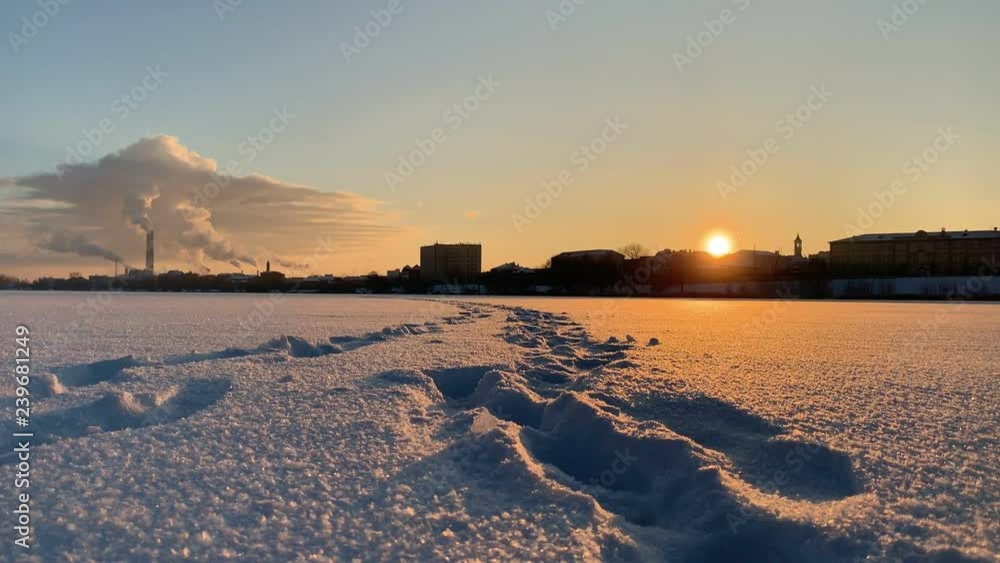 A winter city overview. Frozen river covered in snow. Sunset. Feet traces A winter city overview. Frozen river covered in snow. Sunset. Feet traces