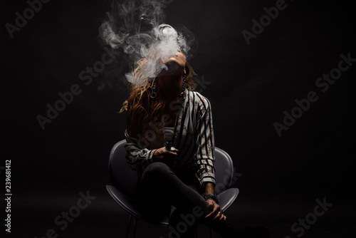 Redhead woman vaping electronic cigarette with smoke on black background closeup. Young woman smoking e-cigarette to quit tobacco. Vapor and alternative nicotine free smoking concept, copy space  © oes