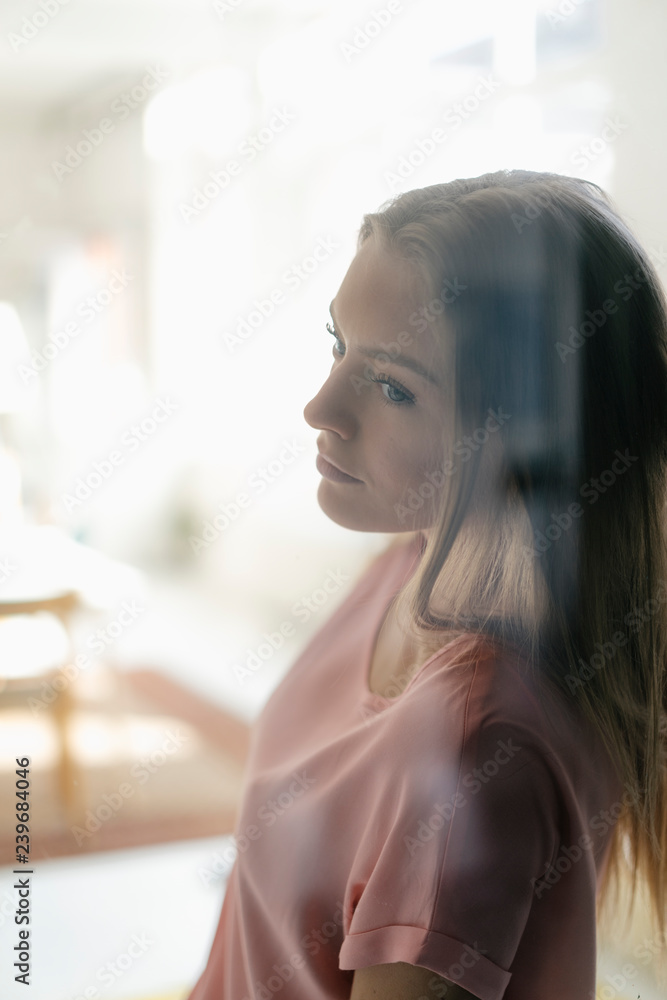 Portrait of pensive young woman behind glass pane