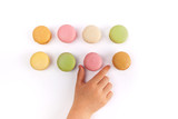 Child's hand taking pink French macaron from two rows of colorful macarons isolated on white
