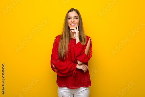 Young girl with red dress over yellow wall thinking an idea while looking up