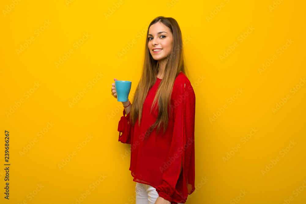Young girl with red dress over yellow wall holding a hot cup of coffee Young girl with red dress over yellow wall holding a hot cup of coffee