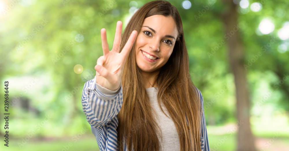 Young girl with striped shirt happy and counting three with fingers at outdoors Young girl with striped shirt happy and counting three with fingers at outdoors