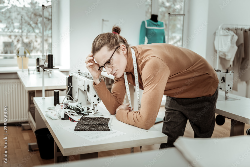 Long-haired fashion dressmaker in a brown garment looking thoughtful