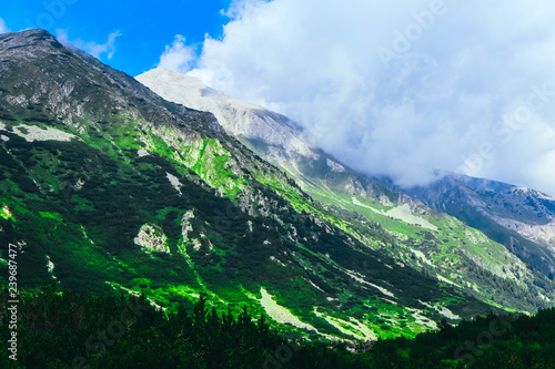 Beautiful alpine high mountains peak, cloudy and foggy. Amazing green hills landscape, summertime.