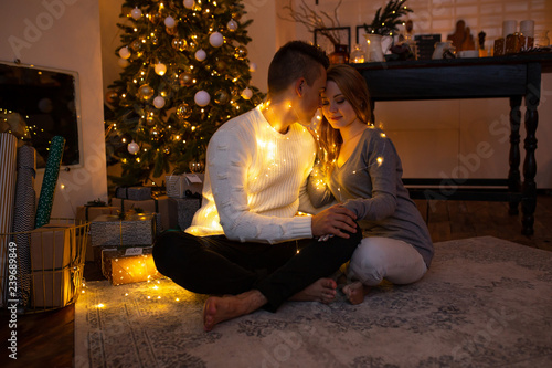 Couple in love sitting next to a Christmas tree. Magic light