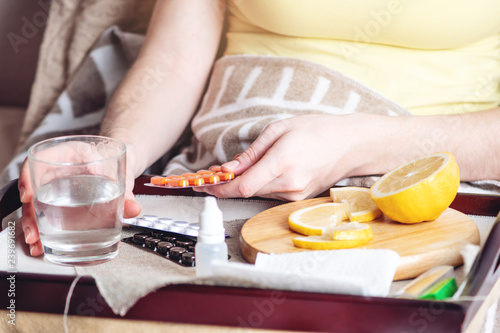 Thermometer pills water and lemon on tray. Person with a cold is treated in bed. Colds, flu and treatment